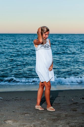 A vertical shot of a Hispanic pregnant woman on the beach at sunset