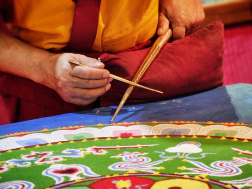 A closeup shot of a Buddhist monk create mandala with multicolor sands