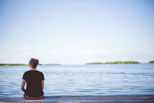 A female sitting on a wooden pathway near the sea with a blurred background shot from behind