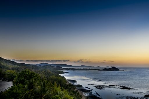 A high angle shot of a beautiful sea near forested mountains and a blue sky in the background