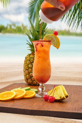 A vertical closeup of a glass of cocktail with a slice of lemon pineapple near, beach blurred background