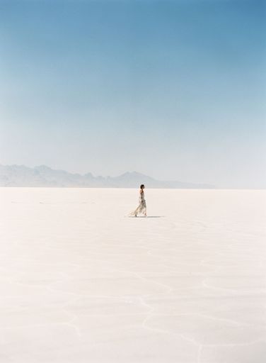 A lady walking in the desert alone under the sunny sky with foggy mountains, vertical shot