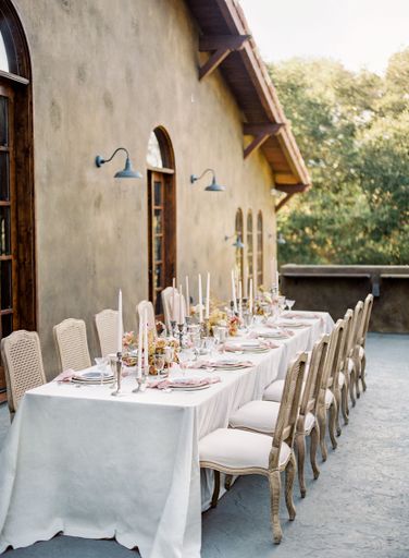 A wedding reception table with white cloth cover by a rural wooden house