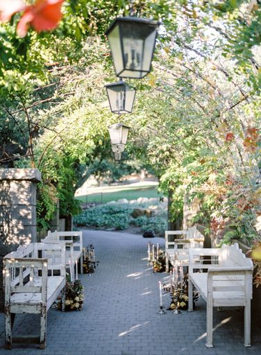 A tiled floor path between wooden seats under an arch plant gate with Garden lanterns, vertical shot