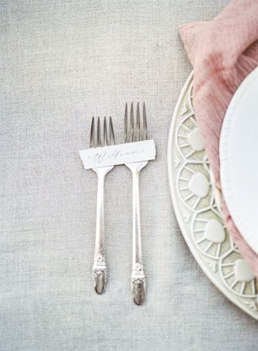 A top view shot of luxury forks next to a ceramic plate on cloth gray surface