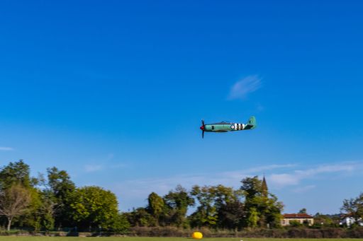 An old helicopter from the Second world war flying over the field with trees in the blue clear sky