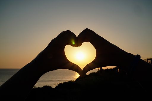 A silhouette of hands forming heart at sunset over Praia do Guincho beach, Portugal