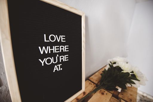 A closeup shot of a sign with love where you're at written on it near a white flower
