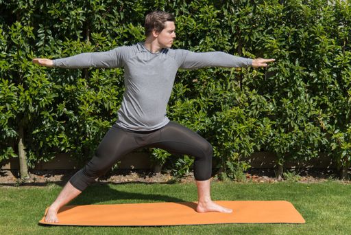 A young fit male practicing yoga and doing the warrior pose outdoors