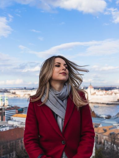 A vertical shot of a young lady in a red suit wit a city port on the background
