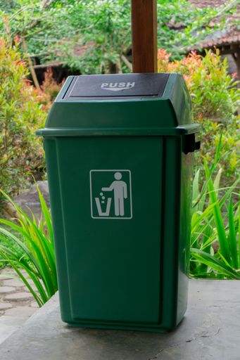 A vertical closeup of a green garbage can in the garden.