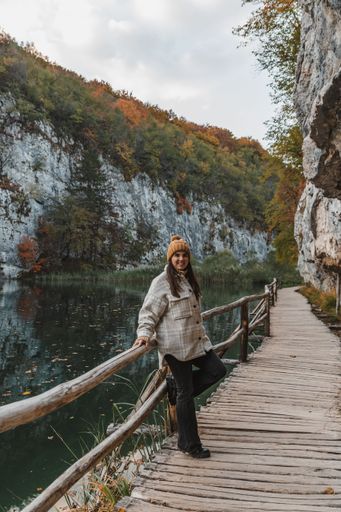 Girl wearing autumn clothes and knitted hat, standing on wooden walkway by a lake in Plitvice lakes national park in Croatia