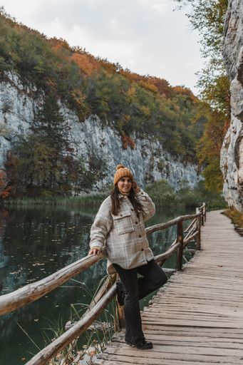 Girl wearing autumn clothes and knitted hat, standing on wooden walkway by a lake in Plitvice lakes national park in Croatia
