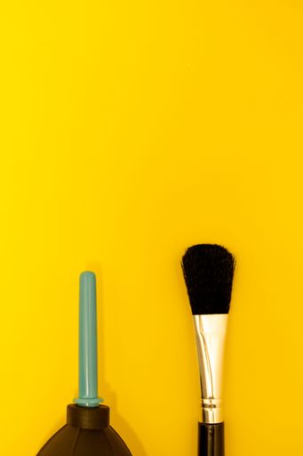 An air pump and brush for clean camera lenses, view from top, yellow background