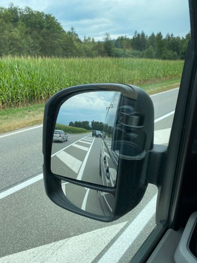 A vertical shot from a car's side mirror with the reflection of the street, with green grass in the background