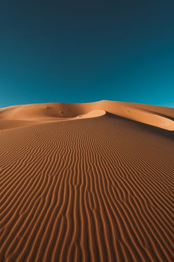 A vertical shot of a peaceful desert under the clear blue sky captured in Morocco