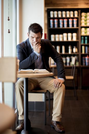 A vertical shot of a well-dressed male sitting in a cafe and reading the bible