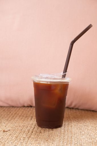 A vertical shot of a coffee cup with a black straw on a pink background