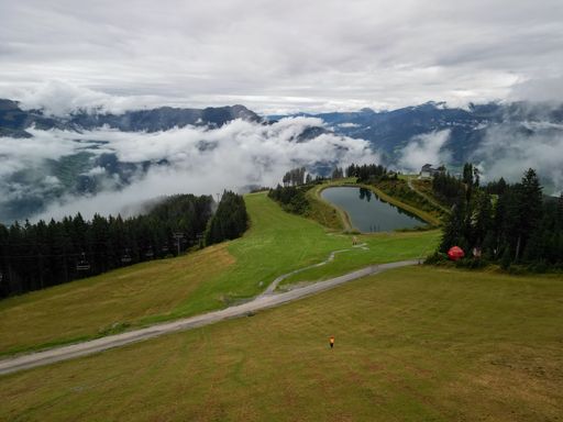 An aerial drone view of a small lake in Austria surrounded by mountains covered by clouds