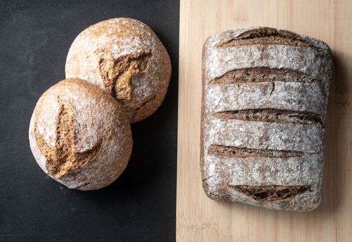 A top view of two types of bread, one on a wooden board, and the second on a black surface