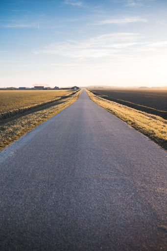 A vertical shot of a straight road under the beautiful blue sky captured in Netherlands