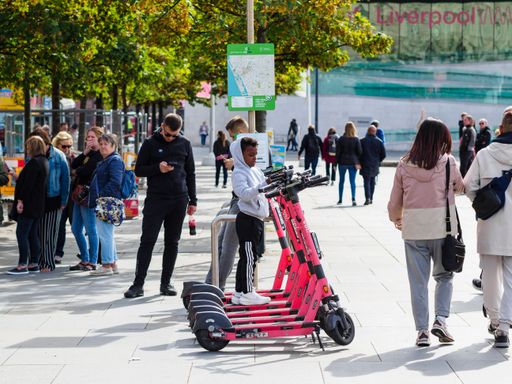 groups of people walking about pier head Alberts dock Liverpool rental electric scooters for hire with small boy trying them out