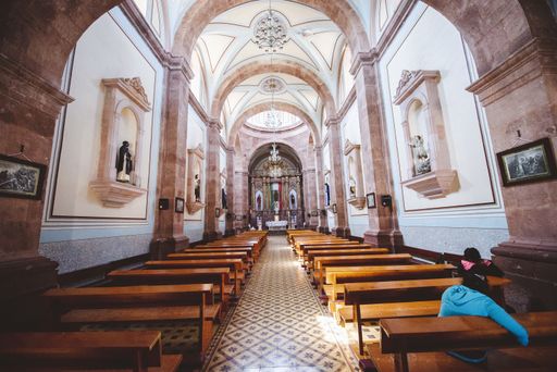 An interior shot of a church with people sitting on the wooden benches