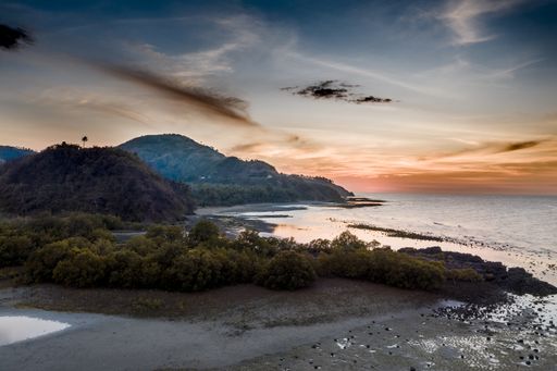 A beautiful shot of forested mountains near the sea under a blue and red sky