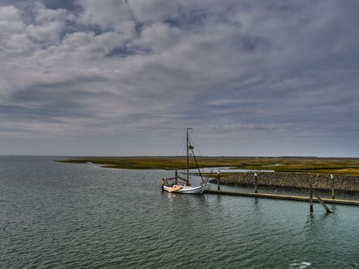 A small rowing boat tied to a pier under a cloudy sky on Spiekeroog island in Germany