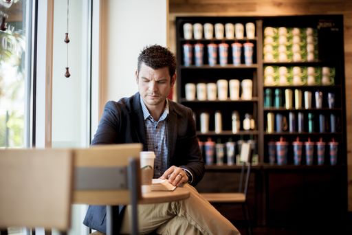 A selective focus shot of a well-dresed male sitting in a cafe while reading the bible