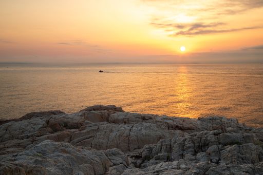 A closeup shot above a rocky cliff and the setting sun coloring the surface of the tranquil sea