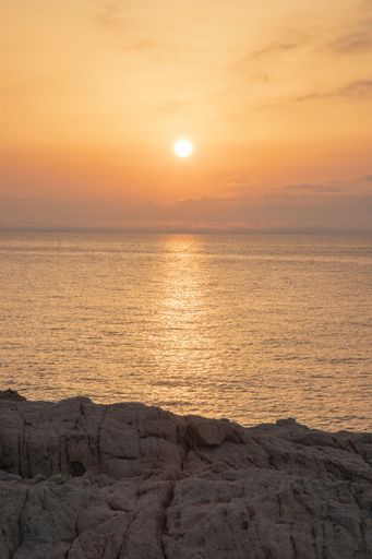 A vertical shot of the setting sun and the orange-colored sky in front of a cliff