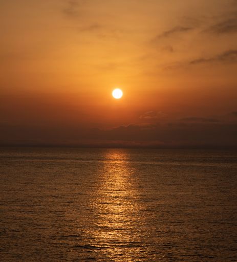 A vertical shot of a vibrant sunset over a tranquil sea on the darkening evening