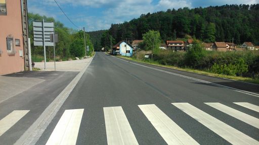 A long empty straight asphalt road in a town with trees on the background during a sunny day