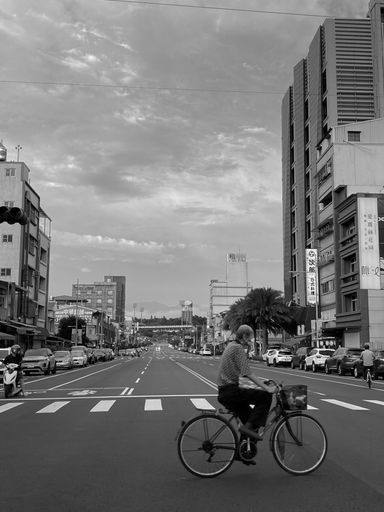 A view of a city street with traffic, with cyclist and tall buildings on cloudy day in Taiwan. Grayscale
