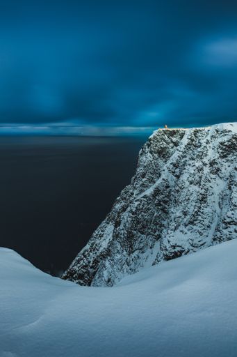 A vertical shot of the breathtaking snow covered mountain peak over the ocean captured in Norway