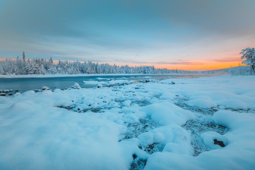 A beautiful lake surrounded by snow covered fields with the trees in the background in Norway