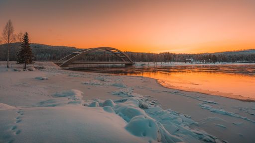 A breathtaking view of a bridge over snow covered field and frozen lake at sunset captured in Sweden