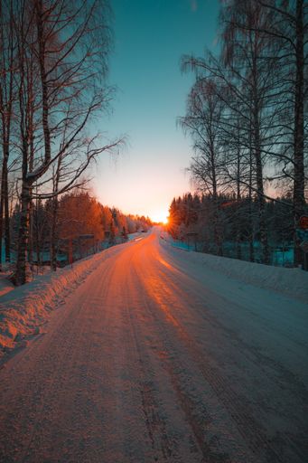 A vertical shot of a snow covered road surrounded by trees captured at sunset in Sweden