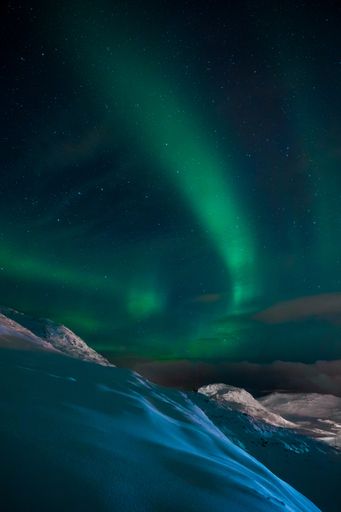 A vertical shot of an aurora in the sky above the hills and mountains covered with snow in Norway