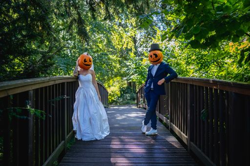 A bride and groom wearing scary pumpkin heads and standing on a bridge