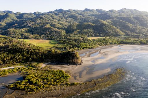 A high angle shot of a sea near a shore and mountains covered in trees at daytime