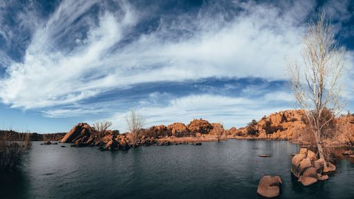 A beautiful view of a lake and rocks on a shore under the cloudy blue sky