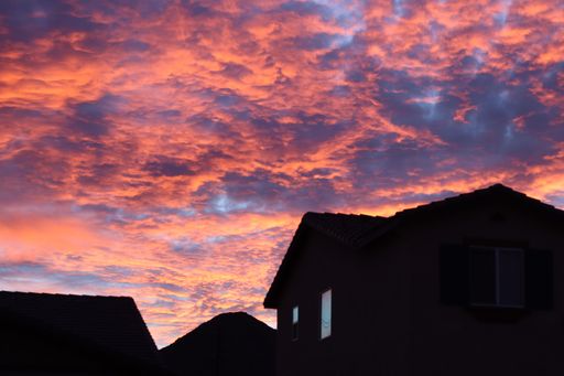 A breathtaking low angle shot of a  gorgeous cloudy sky full of pink, purple and gold clouds over houses