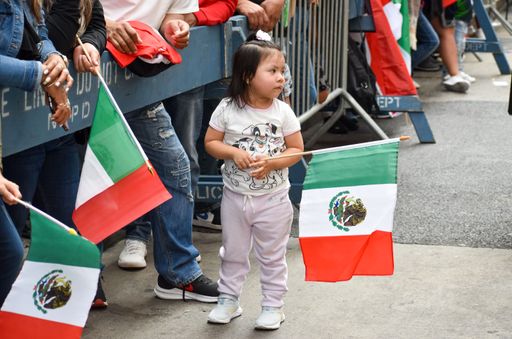 A female child holding a flag on a street during the Mexican Independence Day Parade