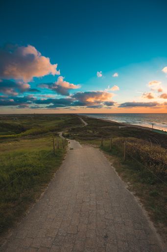 A vertical shot of a paved pathway by the sea under the cloudy sky captured in Domburg, Netherlands