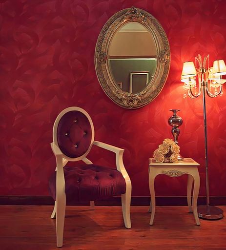 A parquet floor room with an armchair against a red wall with hanging a mirror, lamps and a small table