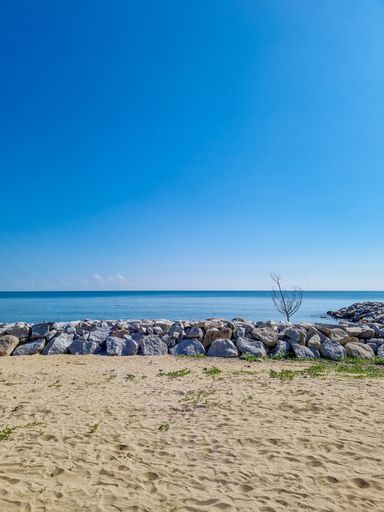 A vertical shpt of a heap of stones on sandy beach by the sea with blue sky n the horizon