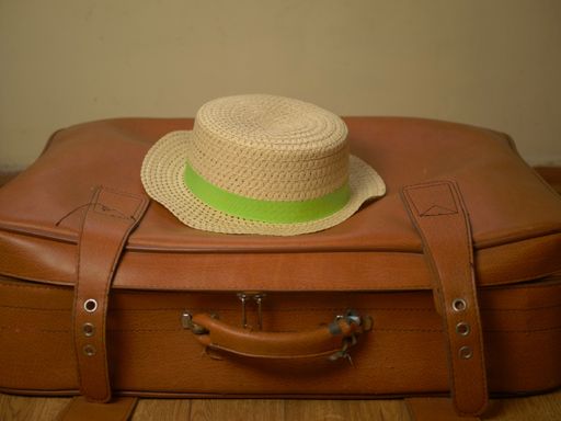 A closeup shot of a brown suitcase with a straw hat