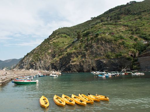 The green Coastal Italian Village Cinque Terre by yellow boats in the water with blue sky
